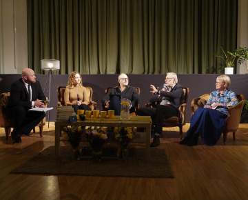 Divas sievietes un trīs vīrieši krēslos diskusiju pasākumā uz skatuves