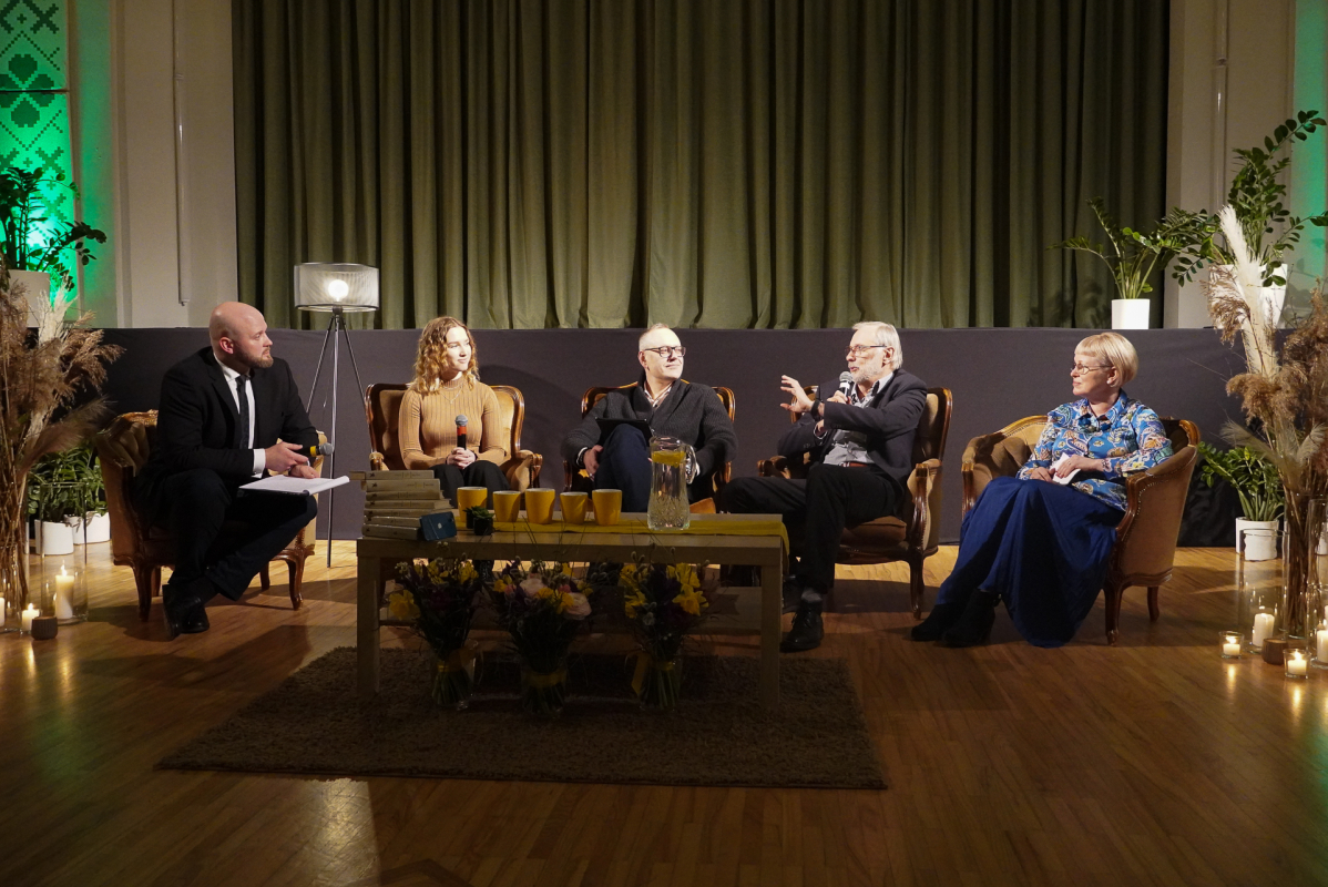 Divas sievietes un trīs vīrieši krēslos diskusiju pasākumā uz skatuves