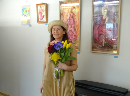 Liena Ivonna Šervinska dzeltenā kleitā ar ziediem un cepuri rokās pie savām gleznām