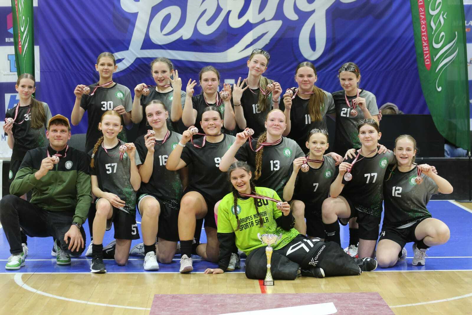 Meitenes ar medaļām kaklā sēž sporta zālē