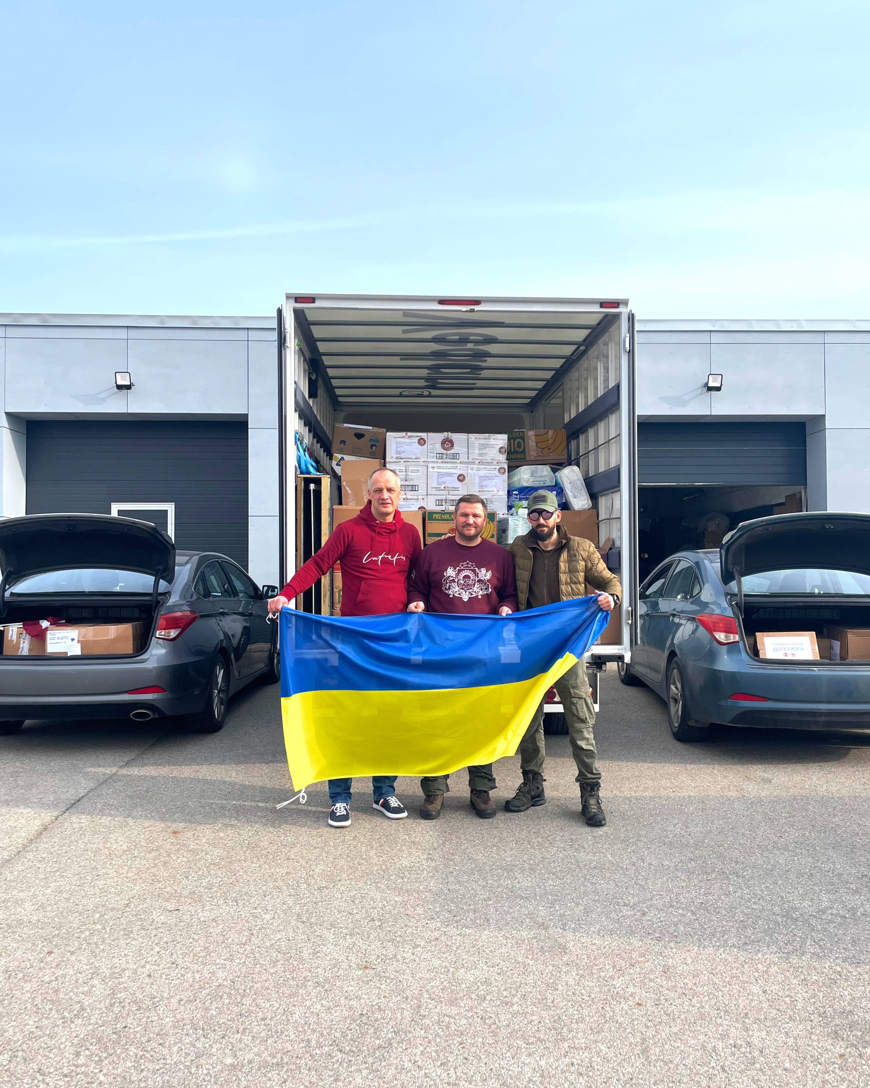 3 vīrieši pie kravas busa ar Ukrainas karogu rokās
