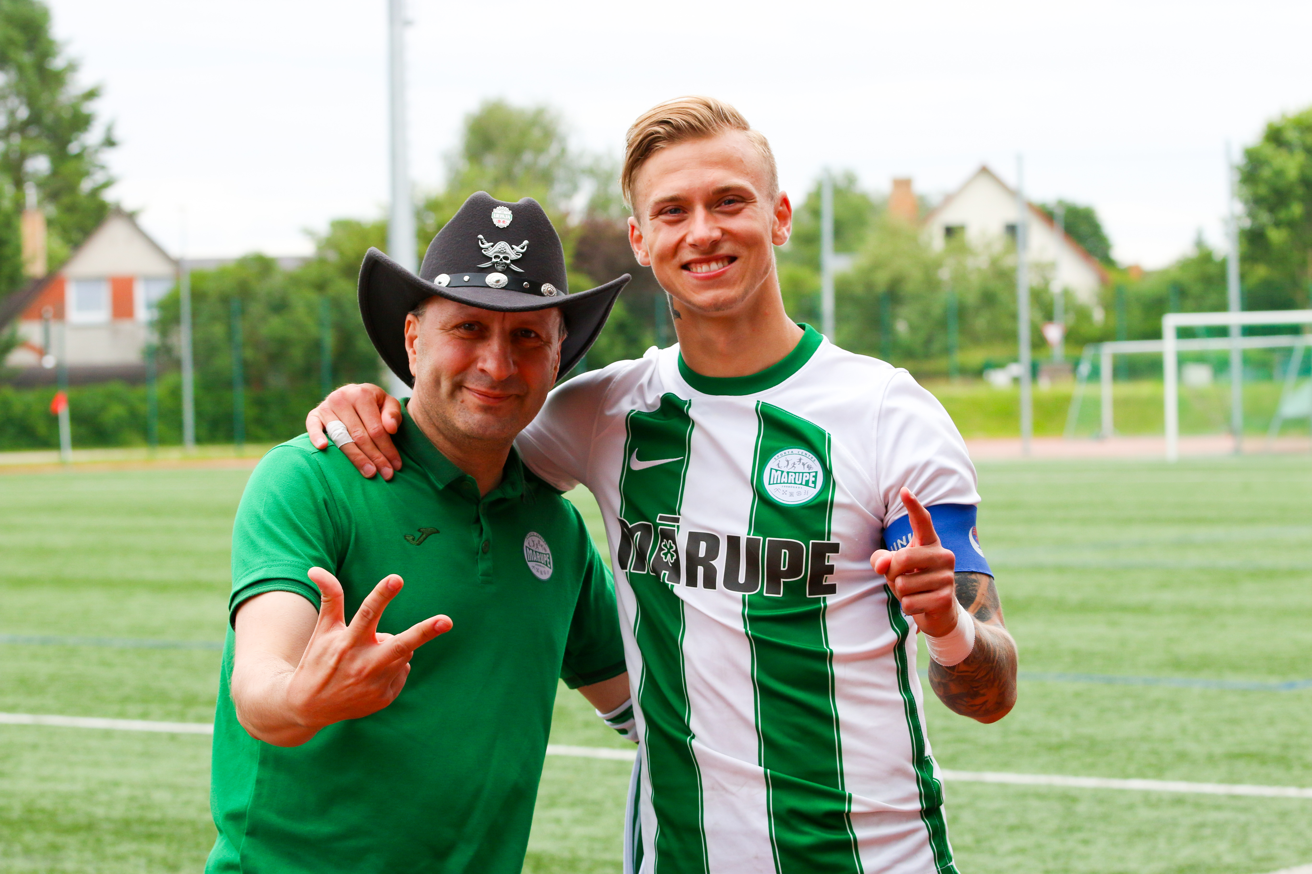 Vīrietis kovboja cepurē kopā ar puisi zaļā sporta tērpā