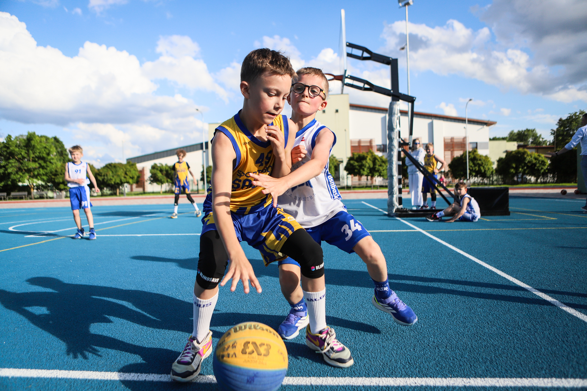 puiši spēlē basketbola uz zila seguma sporta laukumā