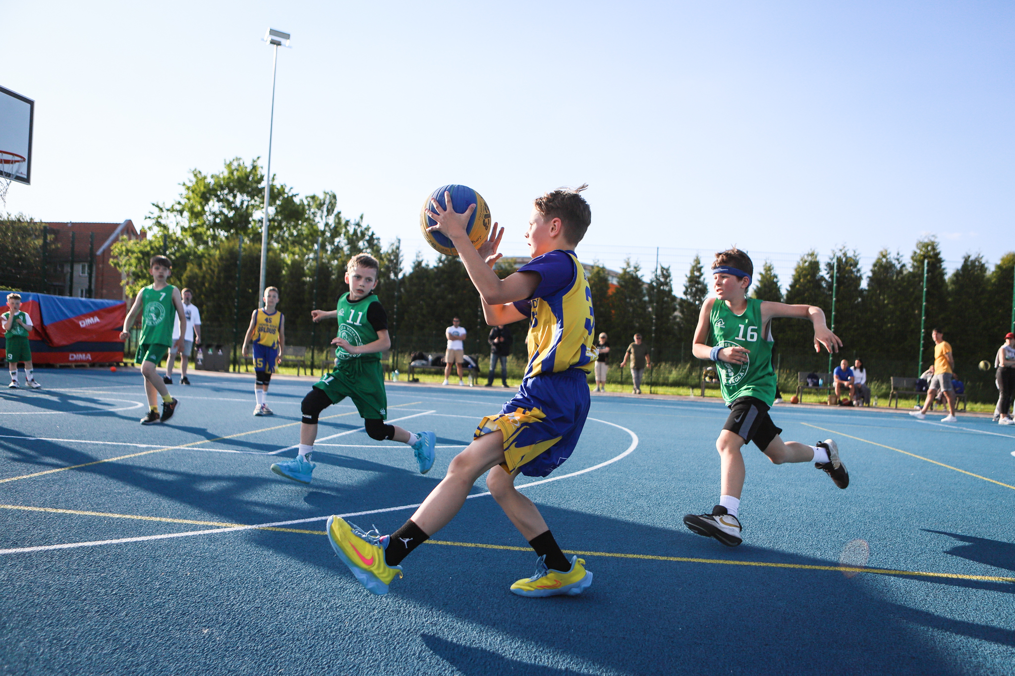 puiši spēlē basketbola uz zila seguma sporta laukumā
