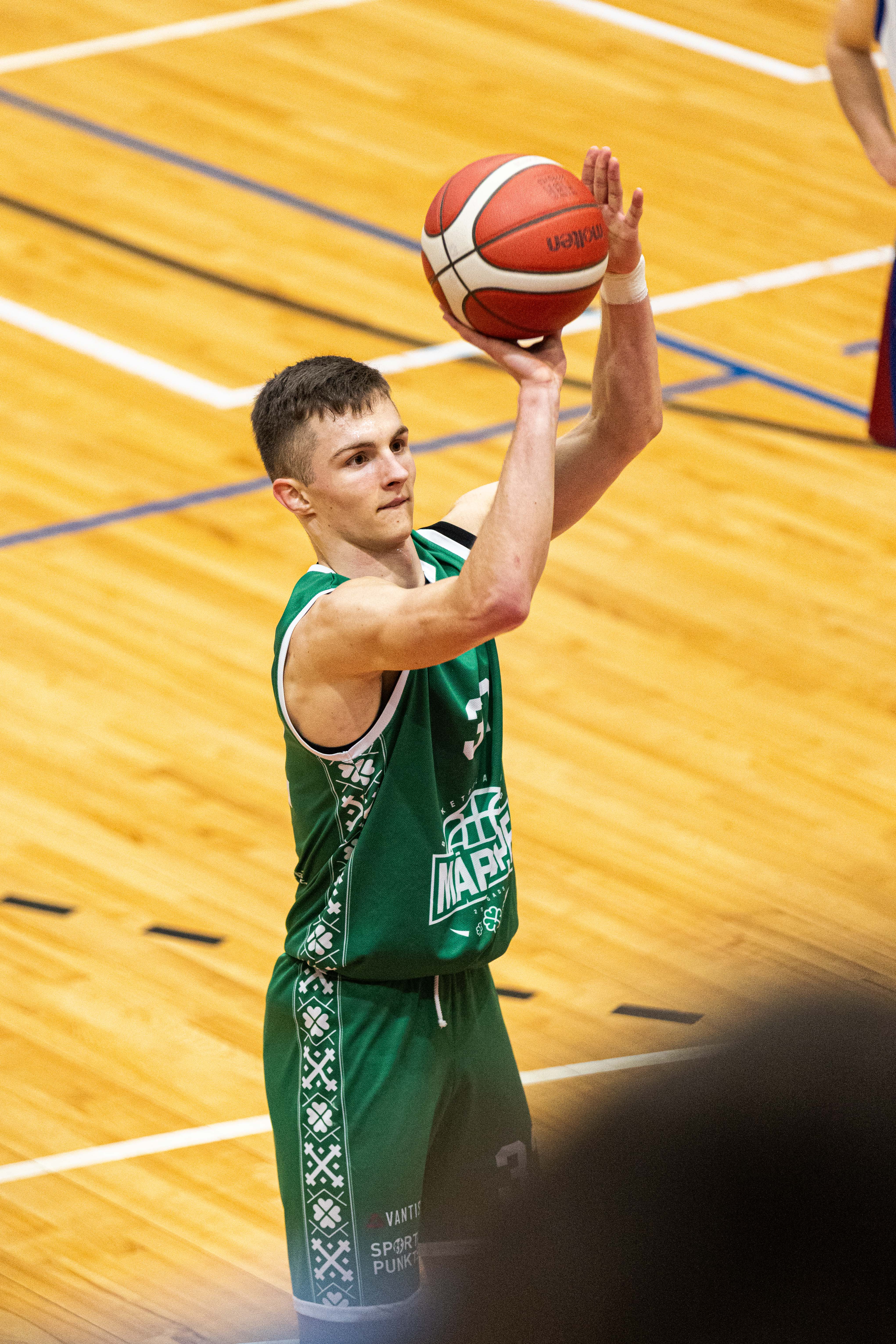 Puisis zaļā sporta tērpā met basketbola bumbu