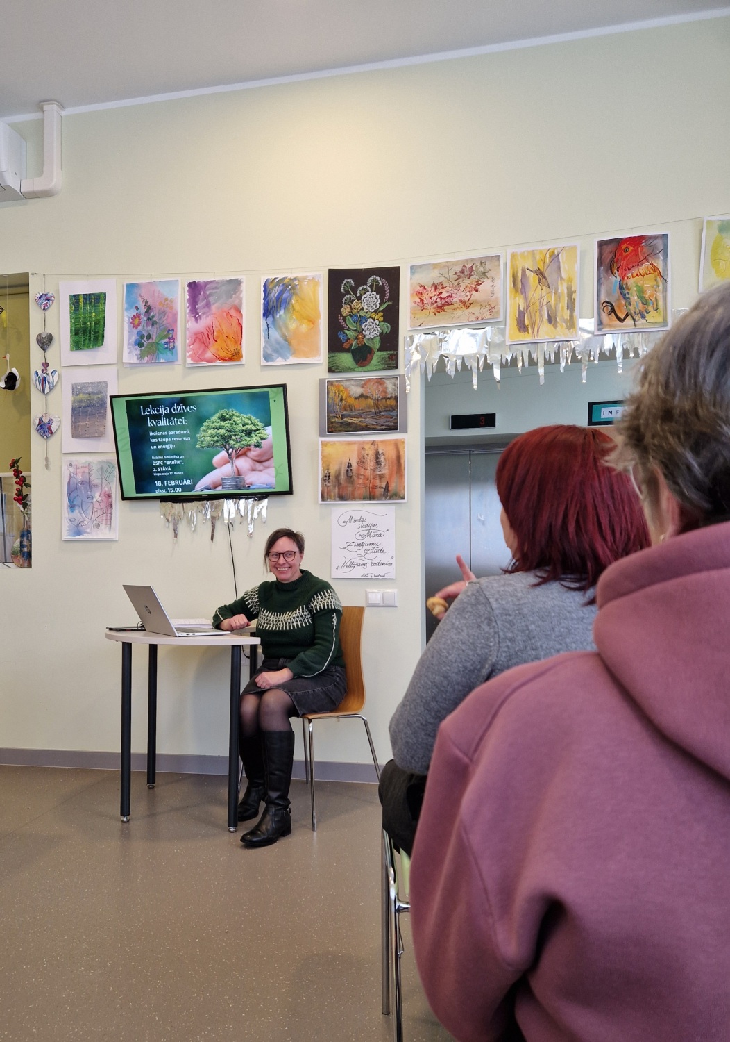 tālskats, redzami lekcijas apmeklātāji no murupuses un priekšā smaidīga lektore