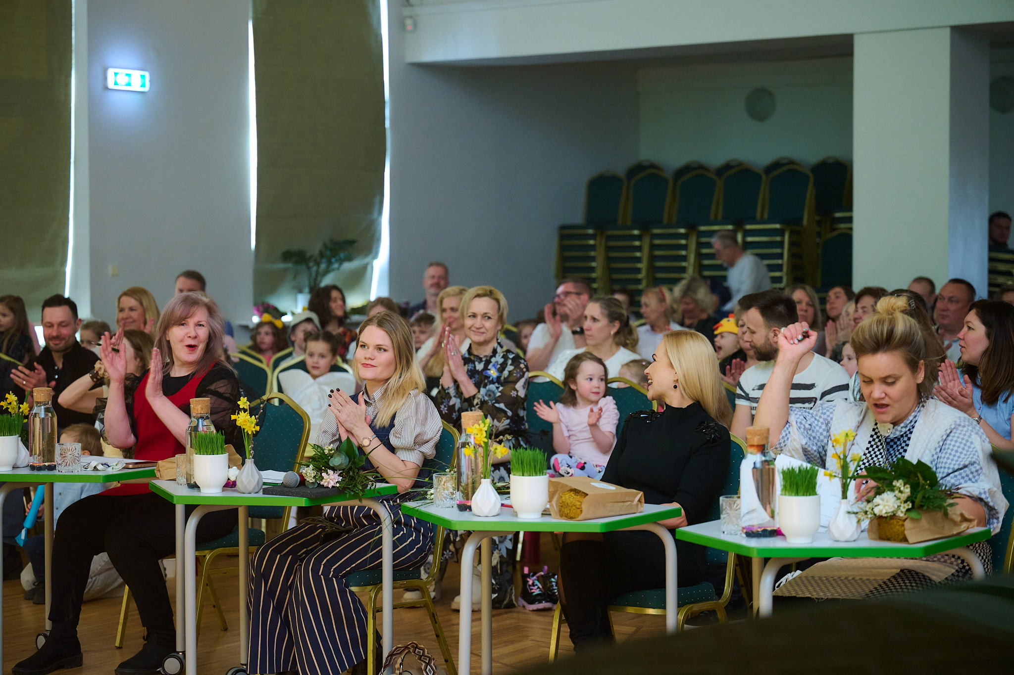 Konkursa žūrijas komisijas locekles pie darba galdiem un aiz viņām skatītāju zāle