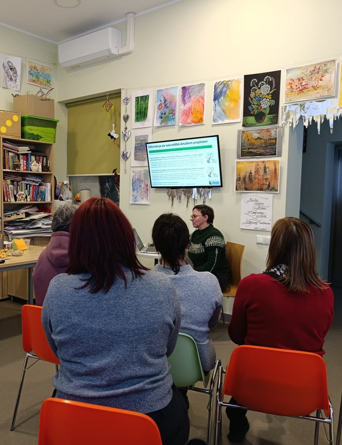 auditorija sēž ar mugurām, priekšā lektors