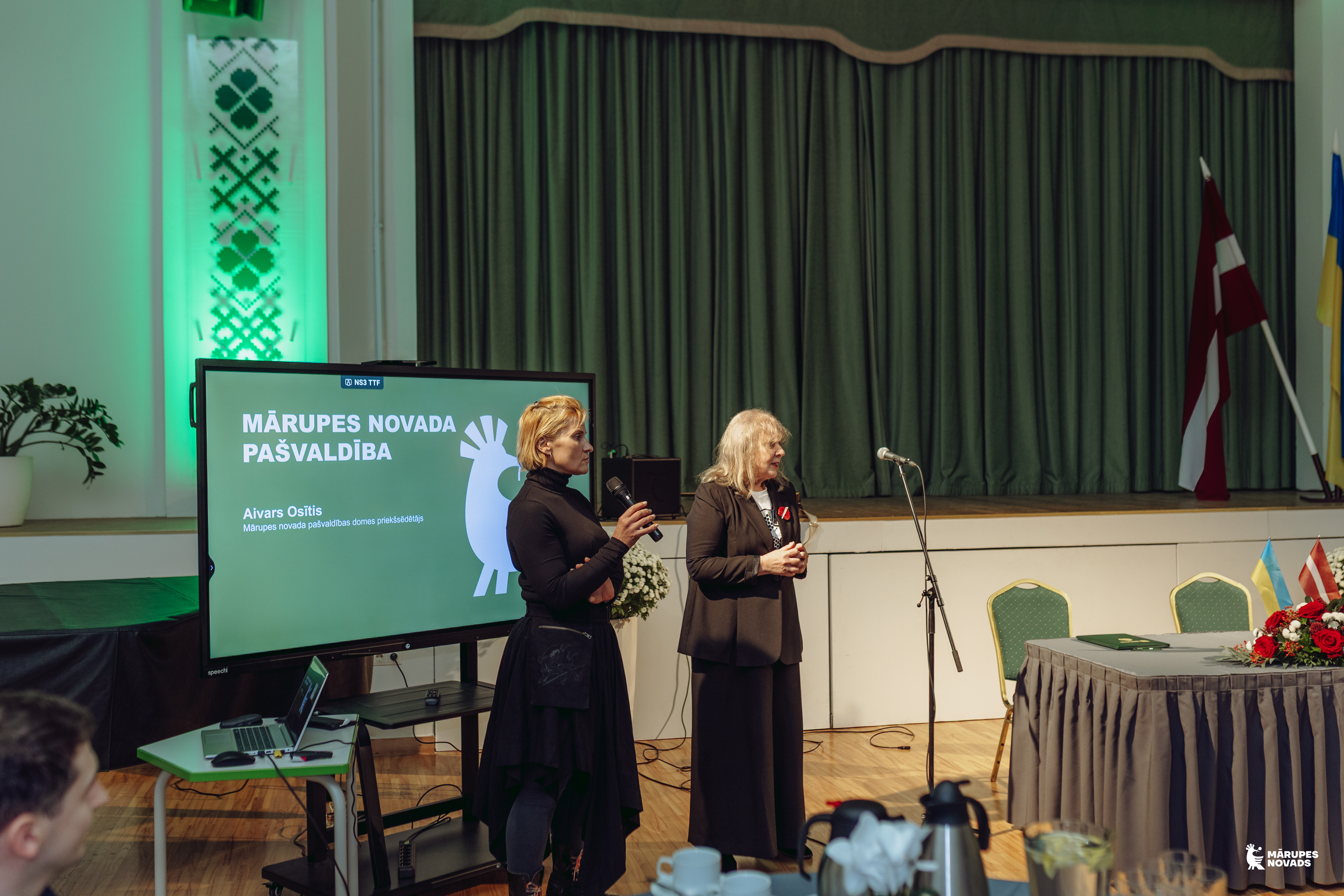 Divas sievietes melnā tērpā svinīga pasākuma zālē