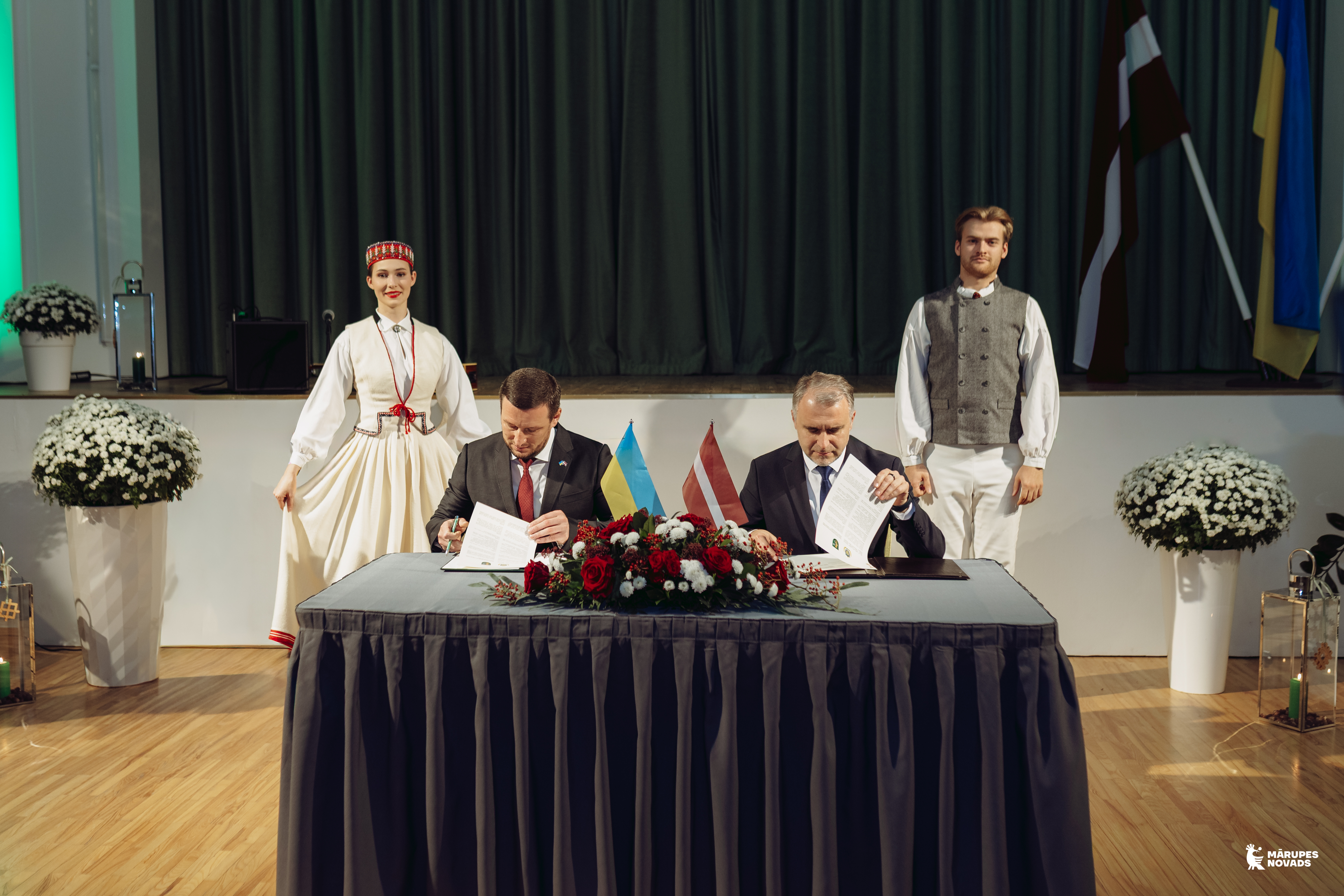 Vīrieši paraksta dokumentus svinīgā pasākumā