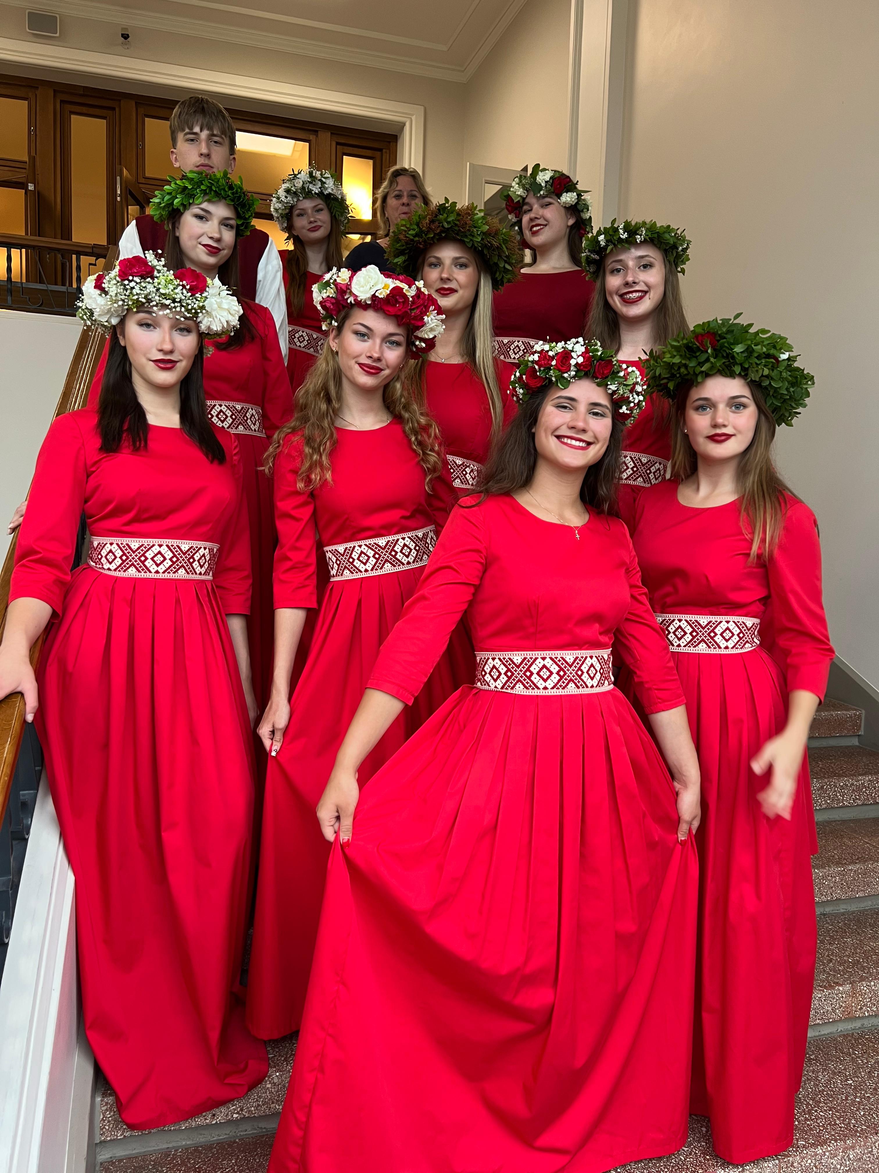 Meiteņu grupa sarkanās kleitās uz kāpnēm