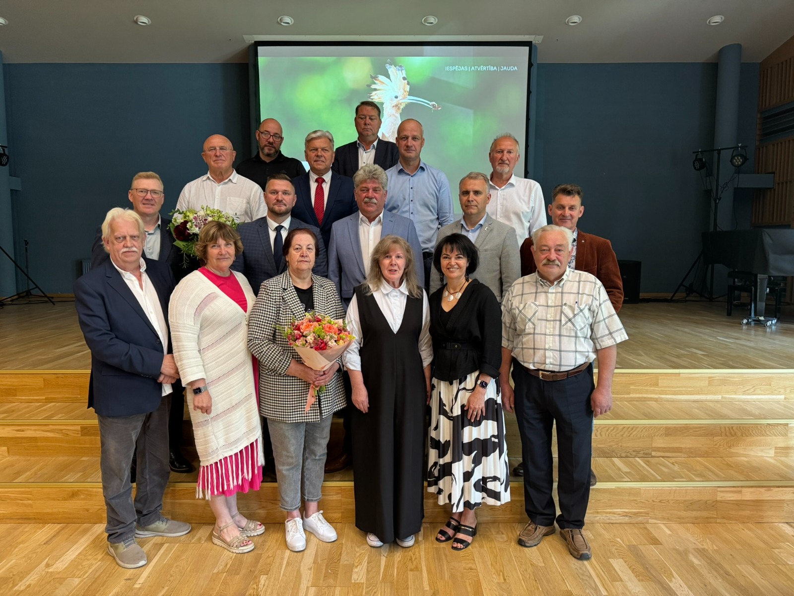 Sievietes un vīrieši uz skatuves ar ziediem rokās