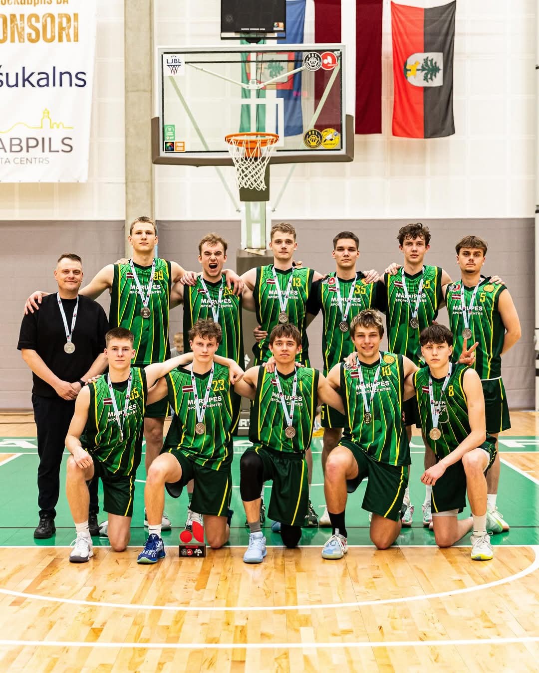 Vairāki sportisti stāv zālē ar sudraba medaļām kaklā