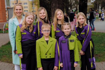 Bērnu popgrupas dalībnieki krāsainos skatuves tērpos ar vadītāju