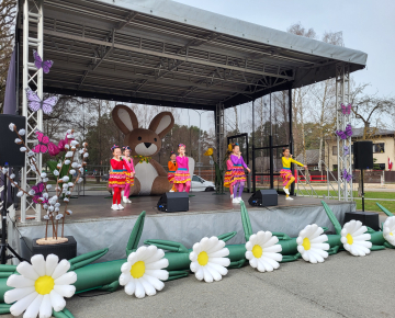 Bērnu popgrupas dalībnieki dzied uz skatuves, kas rotāta ziediem