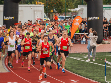 Daudz cilvēku sporta tērpos skrien pa oranžu skrejceliņu