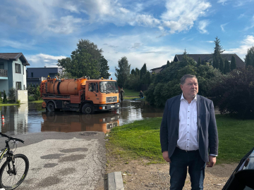 Vīrietis uzvalkā apseko applūdušu ielu krustojumu