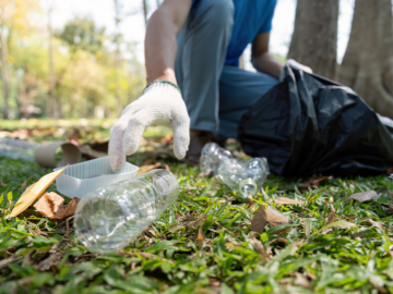 Attēlā cilvēks, kas vāc akritumus - plastmasas pudeles