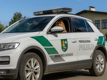 Fotogrāfija ar Mārupes novada pašvaldības policijas automašīnu un pie stūres pašvaldības policijas darbiniece