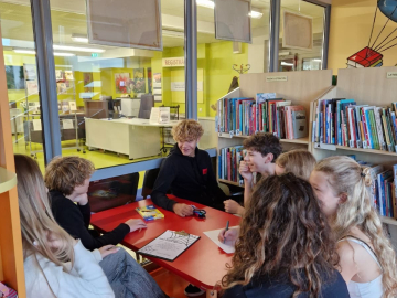 Jauniešu grupa pie galda bibliotēkas telpā