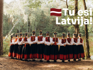 Meitenes tautastērpos zaļā brīvdabā ar baltu teksta grafiku