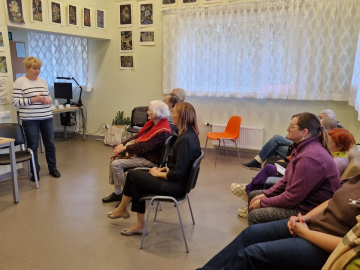 Cilvēku grupa gaišā telpā sēž klausās nodarbību