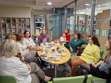 Grāmatu klubiņa dalībnieki sēž ap galdu
