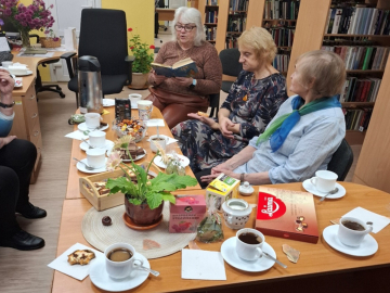 Grāmatu klubiņa tikšanās telpā ar dzeltenām sienām un grāmatu skapjiem