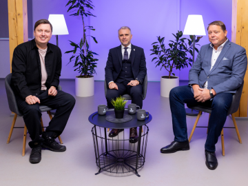 Trīs vīrieši sēž pie melna galda