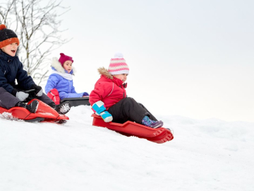 bērni ziemā šļūc ar ragavām no kalniņa