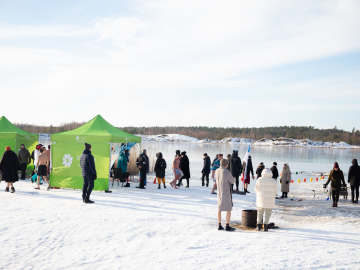 Cilvēku grupa pie aizsalušas ūdenskrātuves ziemas dienā