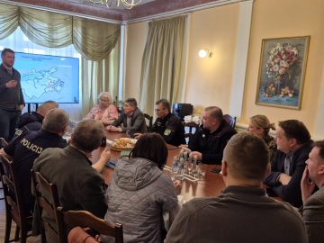 telpa ar galdu, ap kuru sēž cilvēki sapulcē