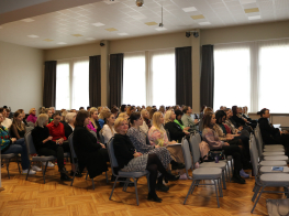 Skats uz zāli, kur krēslos sēž daudz cilvēku, klausoties konferenci