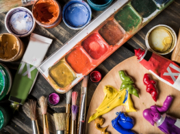 Dažādu krāsu guašas un otas, mākslinieku palete un citi gleznošanas piederumi uz galda