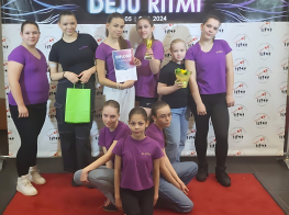 Deju grupas meitenes violetos tērpos uz balta banera