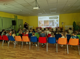 Skolēni sēž krāsainos krēslos un skatās prezentāciju par atkritumu šķirošanu