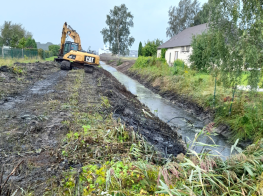 Ūdens noteka, kurai blakus ir dzeltens remontdarbu traktors