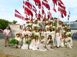 Koris gaišos tērpos pie Latvijas karogiem