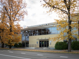 Dzeltena ēka ar stiklotiem logiem, kurai blakus divi koki ar dzeltenām lapām