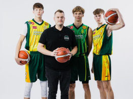 Treneris melnā kostīmā ar basketbola bumbu rokā stāv kopā ar 3 basketbolistiem