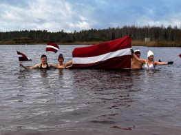 Cilvēki ūdenstilpnē tur Latvijas karogu