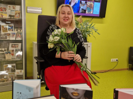 Sieviete sēž krēslā ar ziediem rokās pie koši dzeltenas sienas