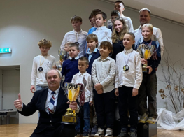 puiši blatos kreklos stāv uz zāles trepēm kopā ar vīrieti melnā uzvalkā un kausu rokā