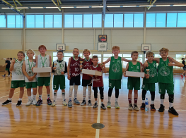 bērni treniņtērpos ar medaļām kaklā stāv rindā sporta zālē