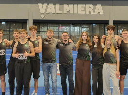 Jaunieši telpās, kur fonā redzams uzraksts "Valmiera"