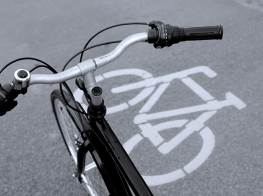 Pelēks betona ceļš ar baltu velo zīmi un velosipēda stūres fragments