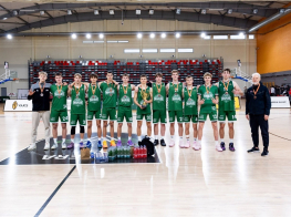 Puiši zaļos sporta tērpos ar medaļām kaklā stāv basketbola zālē