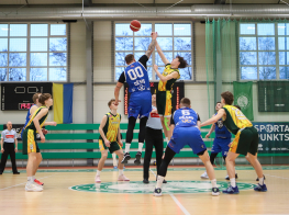 Baketbolisti dzeltenos un zilos kreklos cīnās par bumbu sporta zālē