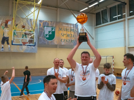Vīrietis baltā kreklā tur kausu virs galvas sporta zālē