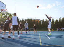 Vīrieši uz zila seguma sporta laukumā spēlē basketbolu
